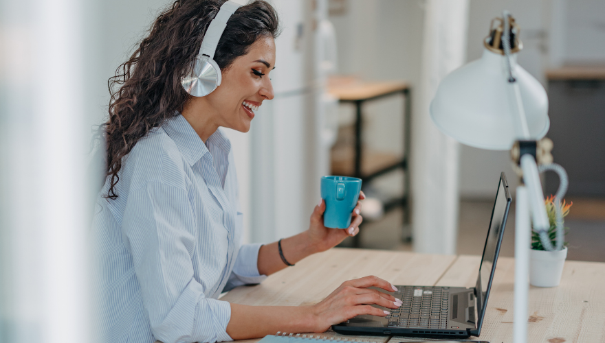 Woman drinks coffee while watching webinar on laptop.
