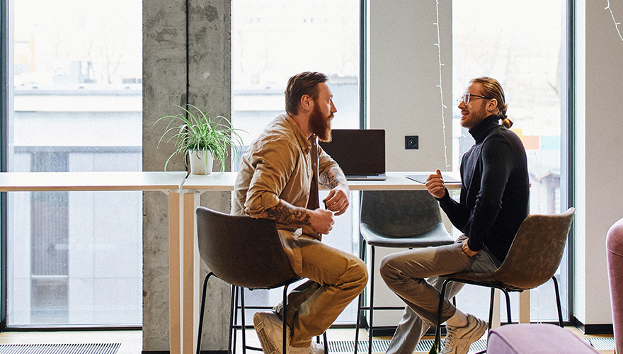 Two Caucasian males sitting on stools in a modern office environment.