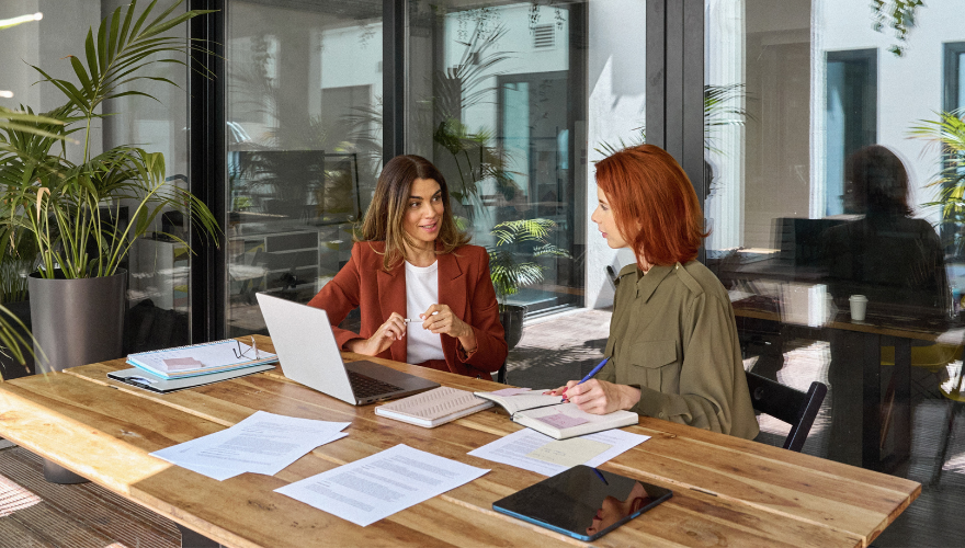 Two businesswomen review paperwork in modern office.