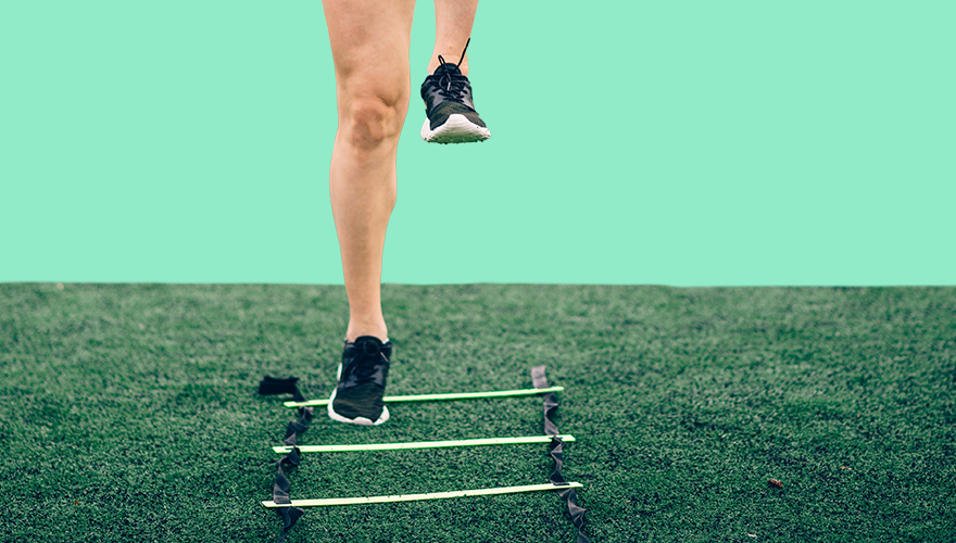 An athlete running drills with a ladder on the floor of the field