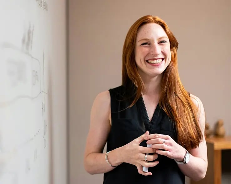 A photo of a smiling woman in front of a whiteboard