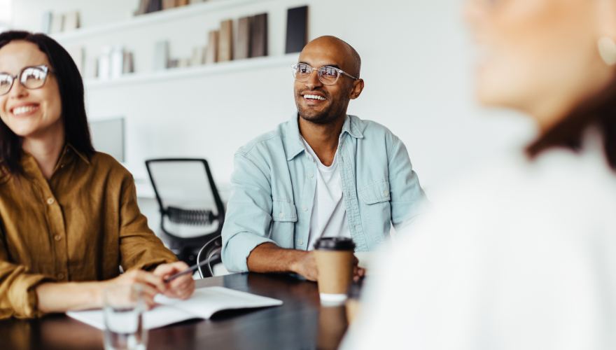 Man with a coffee cup at an office with a coworker listening during a meeting