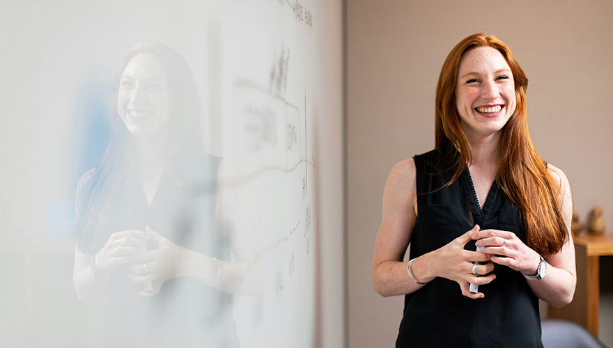 A photo of a smiling woman in front of a whiteboard