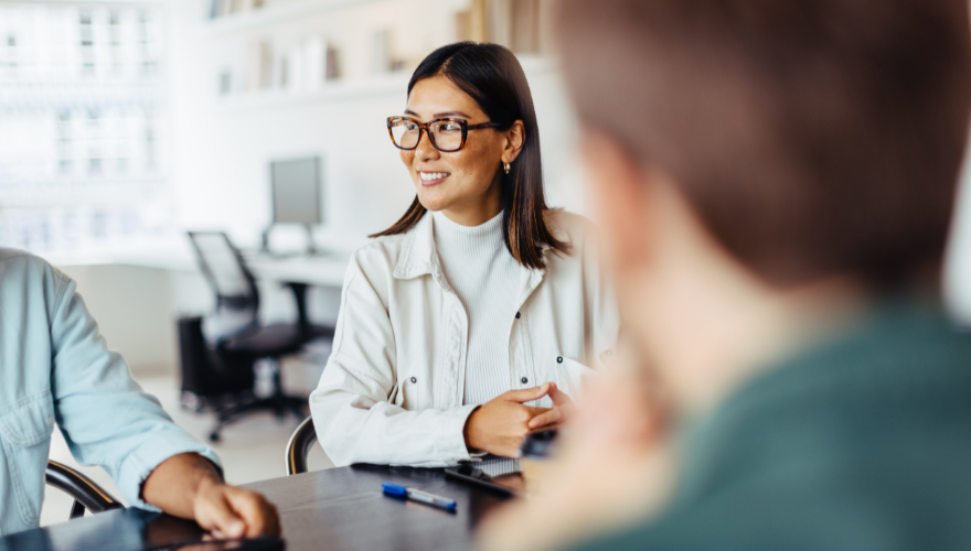 A woman with glasses smiling during an office meeting with coworkers